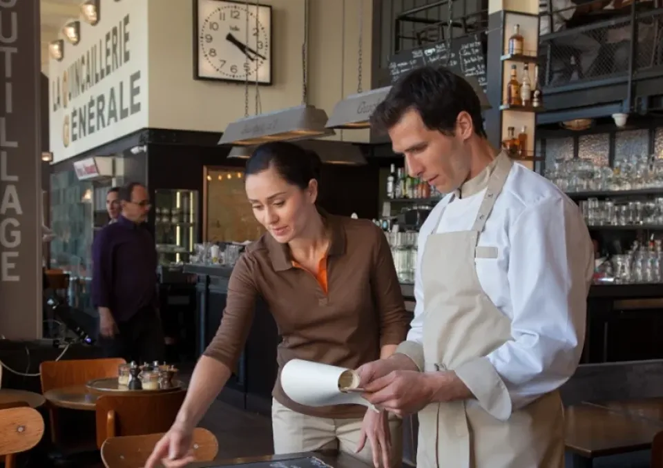 Deux personnes, une personne portant une tenu de service de restauration, une autre portant une tenu de cuisine